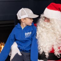 Little boy in blue zip up and grey GVSU hat looks at Santa